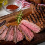Sliced tri tip seak marinated with santa maria sauce on a wooden cutting board.