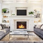 A white living room with a couch on either side of a fireplace that has a TV mounted above it.