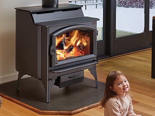 little girl sitting infront of wood stove