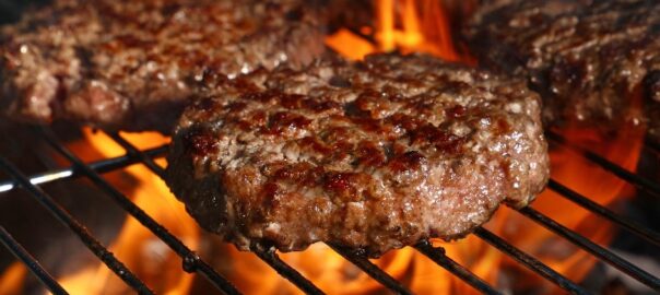Burgers being grilled over wood chips and charcoal