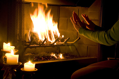 A person holds their hands over a wood fireplace to warm up while candles add to the ambiance