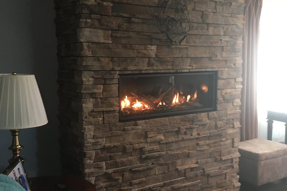 A fireplace insert in a brown, stone setting that extends from the floor to the ceiling