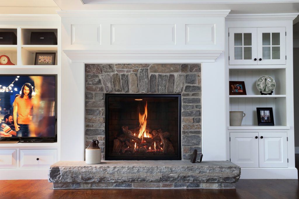 A fireplace insert in a gray stone setting, surrounded by white shelving