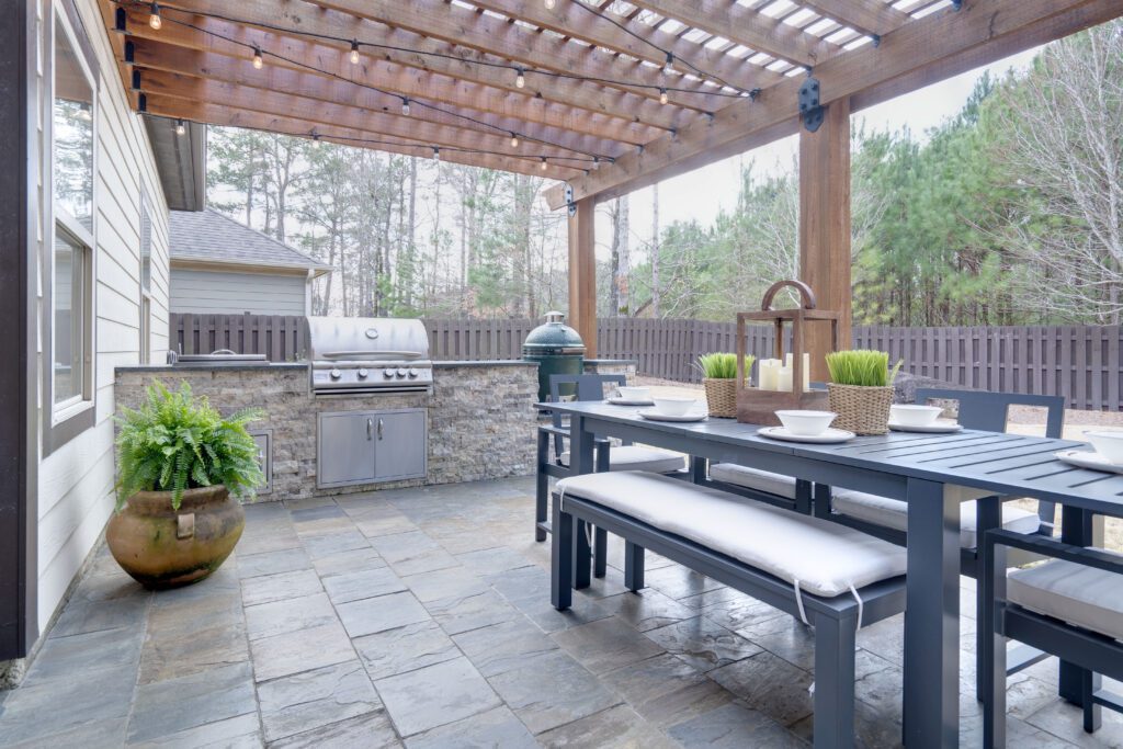 An image of a covered outdoor kitchen with a stainless steel grill and a small table with gray chairs.
