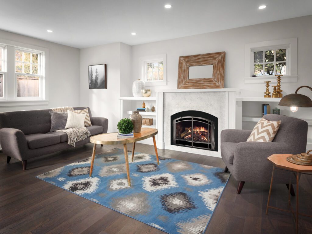 a living room with gray couches, a wooden table, a gas fireplace, and a blue carpet