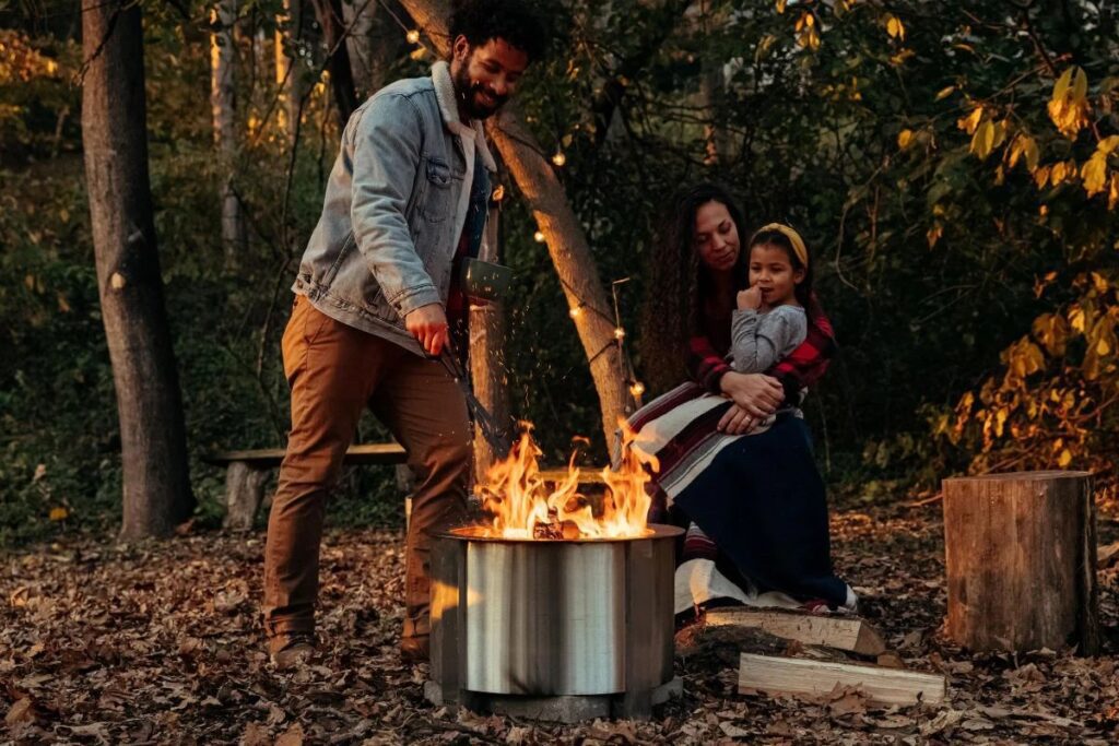 A family sitting around a Breeo, with one person tending to the fire.