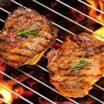 Grilled pork steaks on a flaming grill.
