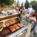 People gathered at a bar, overlooking a person cooking at a grill.